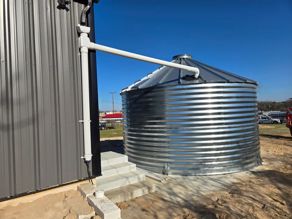 Metal rainwater tank connected to roof capture plumbing beside a Texas building